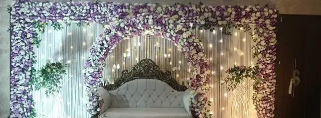Stage backdrop in white and purple flowers with fairy lights and a carved sofa